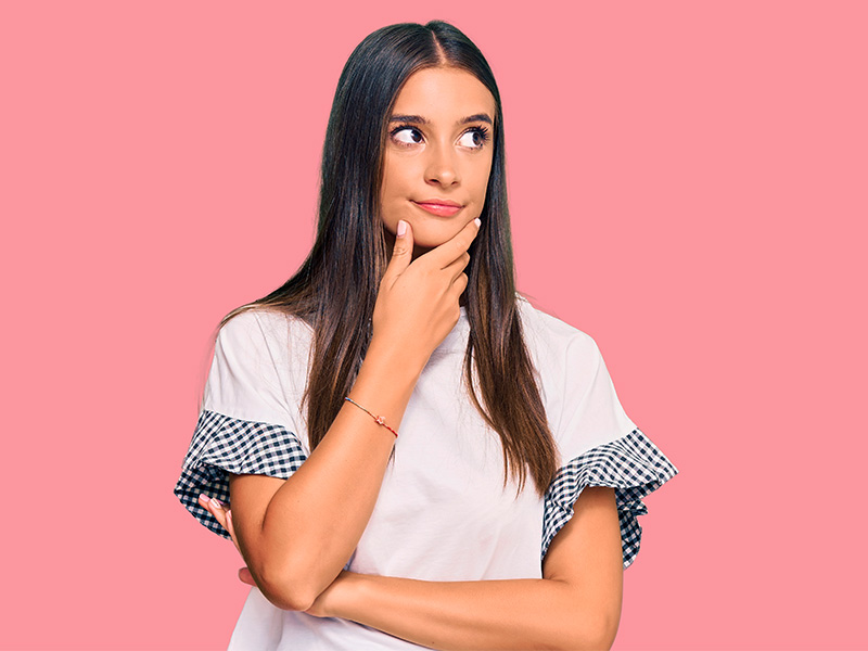 Como funciona a cirurgia combinada? Mulher em um fundo rosa com a feição pensativa se questionando sobre a cirurgia plástica tripla