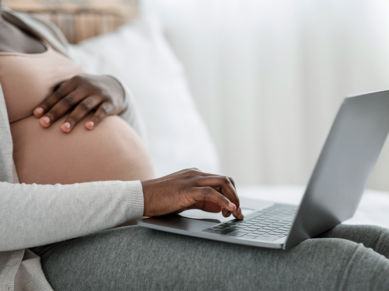 Mulher grávida, sentada com o notebook no colo, pesquisando quanto tempo depois do parto pode fazer cirurgia plástica