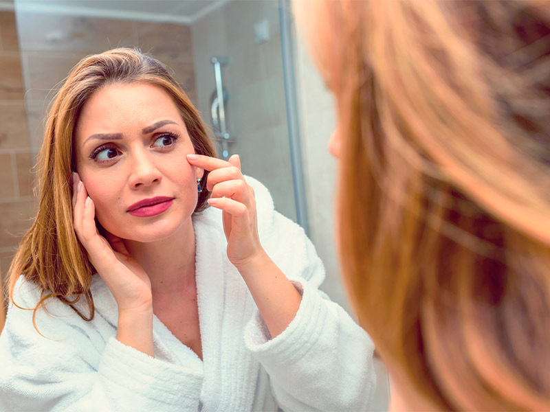 Para que serve o botox? Imagem de uma mulher se olhando no espelho e cogitando aplicar botox no rosto