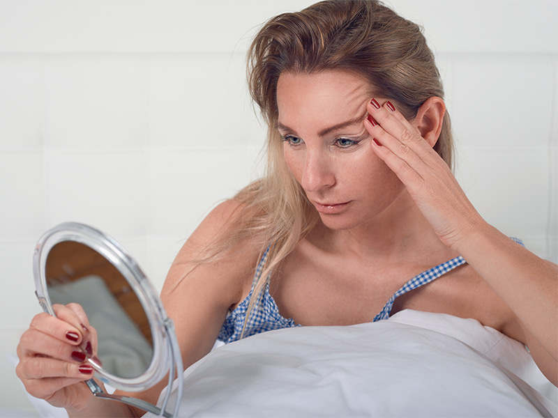 Imagem de uma mulher se observando no espelho e pensando sobre os benefícios do botox para a pele