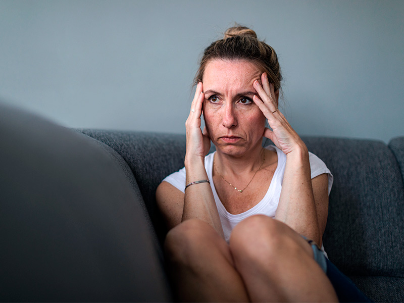 Mulher sentada no sofá com as mãos na cabeça pensando sobre o antes e depois do botox