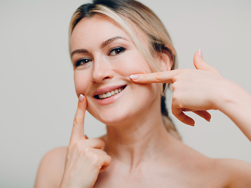 Imagem de uma mulher sorrindo e tocando com os dedos indicadores a região onde se forma o bigode chinês