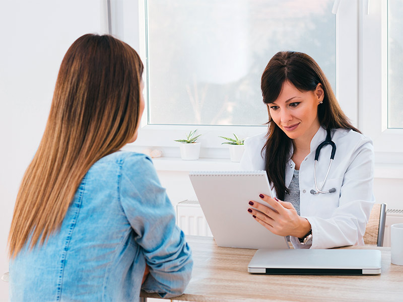 Médica lendo em um caderno sobre quem pode fazer mentoplastia para uma paciente em consulta