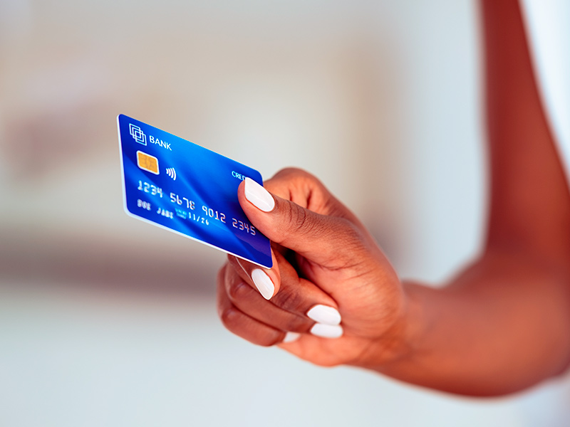 Mão com esmalte branco segurando um cartão de crédito para pagar o valor da cirurgia nos flancos