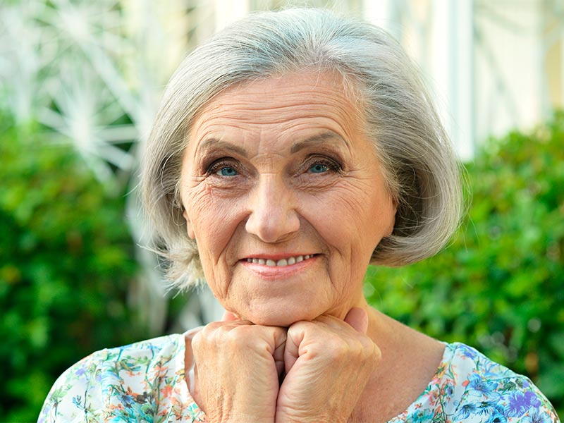 Imagem de uma mulher idosa sorrindo e as rugas estáticas em seu rosto são destacadas