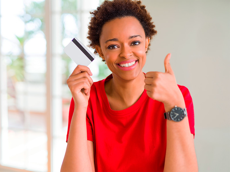 Mulher de camiseta vermelha, segurando um cartão de crédito, fazendo um joinha e sorrindo com o preço para a cirurgia plástica para remover cicatriz 