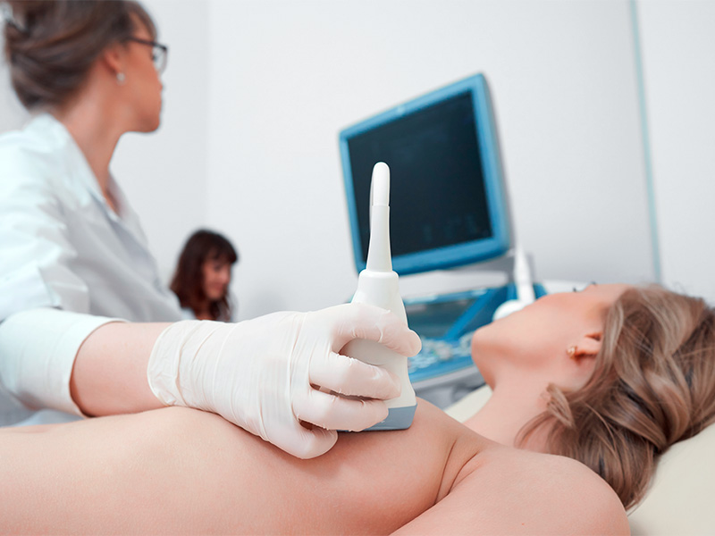 Médica fazendo ultrassom nos seios de paciente deitada na maca