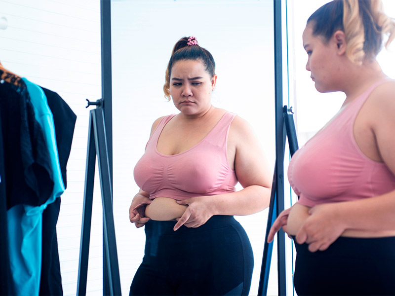 mulher pensando em fazer abdominoplastia acima do peso enquanto se olha no espelho