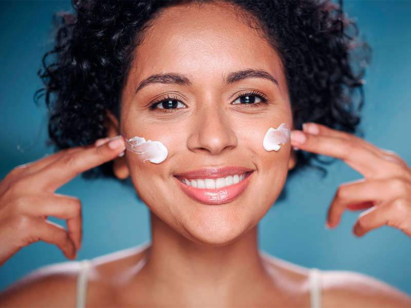 Mulher sorridente passando protetor solar nas bochechas como cuidados do preenchimento