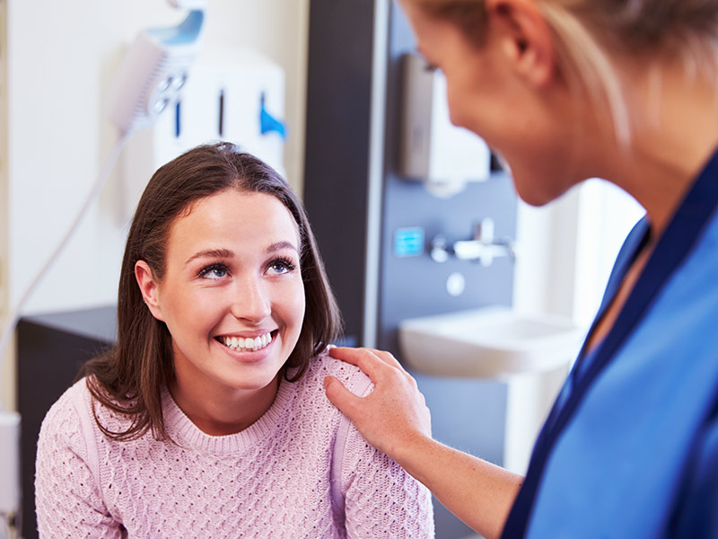 Médica com a mão no ombro de paciente sorrindo