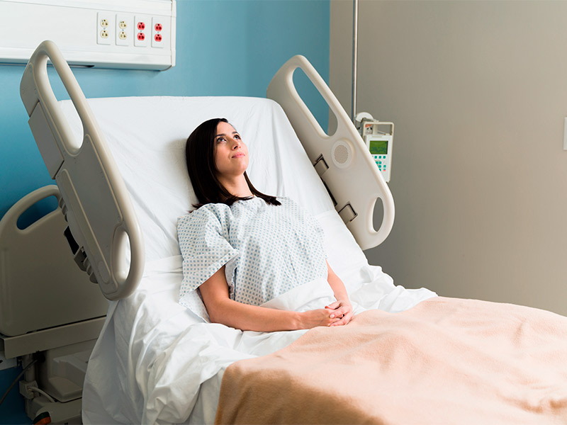 Mulher deitada na cama no hospital, pensando no pôs-operatório da mamoplastia redutora