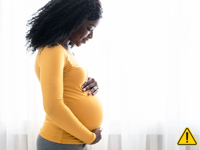 Mulher grávida de lado segurando a barriga e o símbolo de perigo no canto direito da imagem
