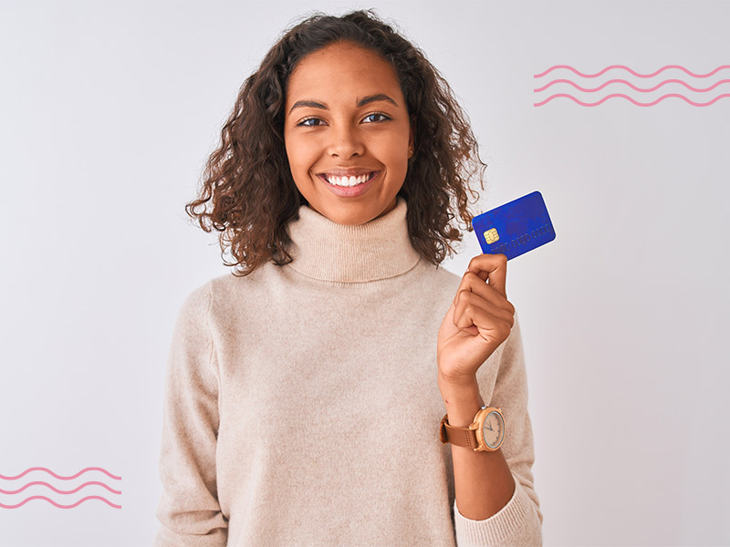 Quanto custa a sessão com o Radiesse? Imagem com fundo cinza e uma mulher no centro, sua expressão é de felicidade e ela está segurando um cartão de crédito para exemplificar qual é o preço do Radiesse