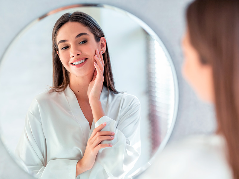 Imagem de uma mulher se olhando no espelho e apreciando o resultado do bioestimulador Ellansé