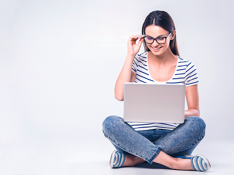 Imagem de uma mulher sentada no chão, com um notebook apoiado nas pernas, pesquisando onde comprar o bioestimulador Ellansé