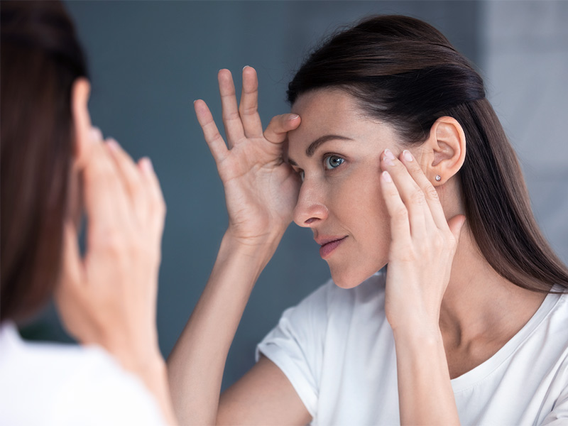Imagem de uma mulher se olhando no espelho e buscando pelos resultados do Radiesse na pele.