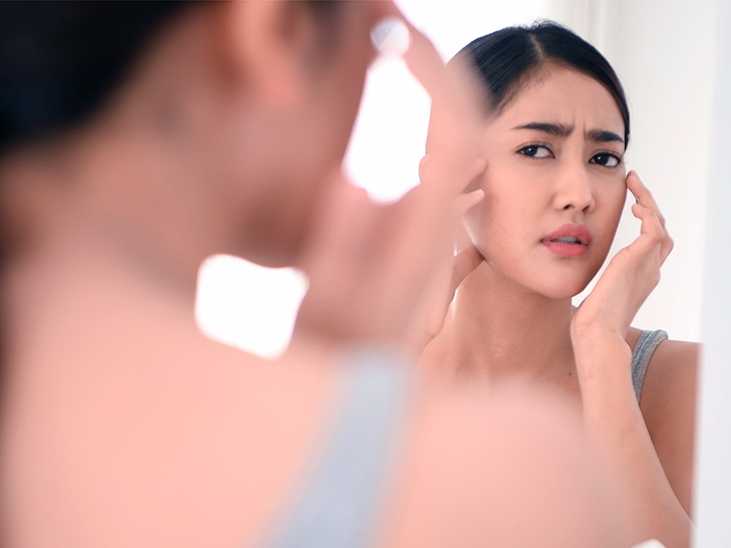 Foto de uma mulher se olhando no espelho e avaliando se gostou do resultado do sculptra no rosto