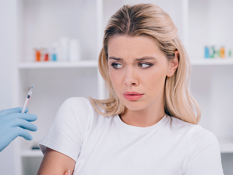 Imagem de uma mulher dentro do consultório, observando uma seringa com expressão de medo devido aos riscos do hidrogel