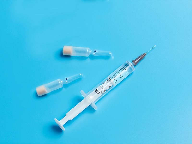 Imagem com fundo azul, uma seringa e duas ampolas exemplificando o ácido hialurônico e a hidroxiapatita de cálcio