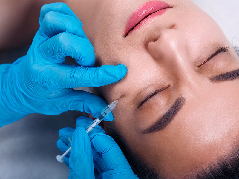 Imagem de uma paciente deitada, dentro do consultório médico, enquanto o profissional realiza a aplicação do pmma em seu rosto