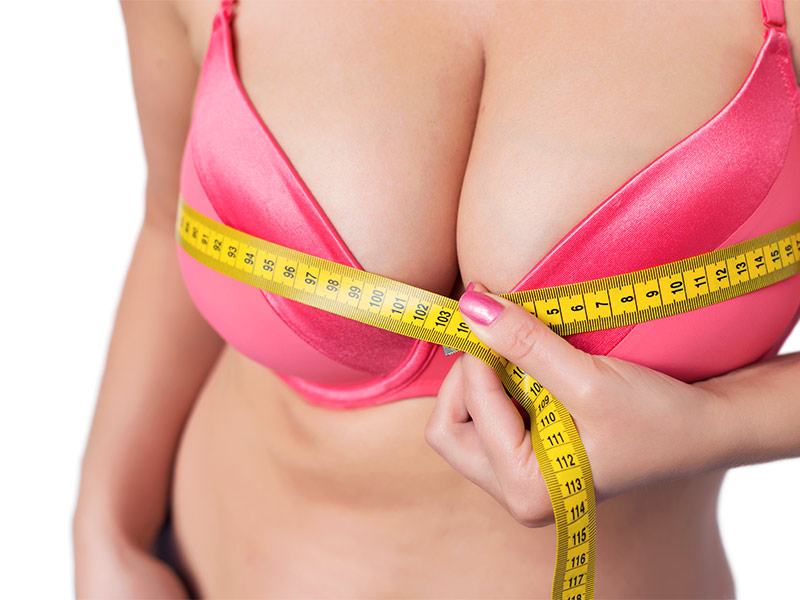 O que é mamoplastia redutora? Mulher de sutiã rosa medindo os seios com fita métrica para saber se precisa de uma mamoplastia redutora
