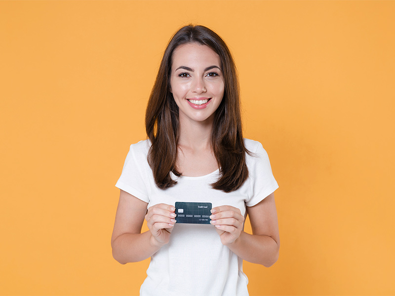 Mulher sorrindo em um fundo laranja com um cartão de crédito na mão perguntando sobre o valor da R24R