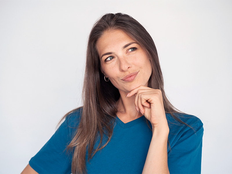 Mulher de camiseta azul com a mão esquerda no queixo, olhando para o lado e pensando na diferença entre mamopexia e mamoplastia