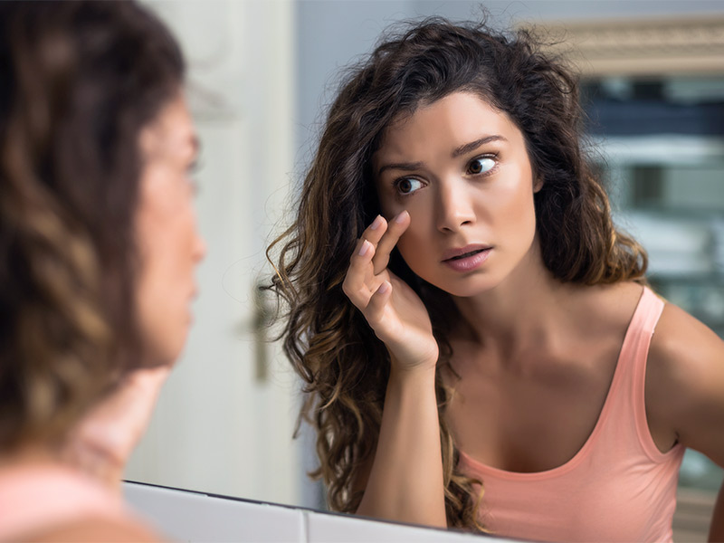 Imagem de uma mulher se olhando no espelho e buscando sinais de envelhecimento em seu rosto