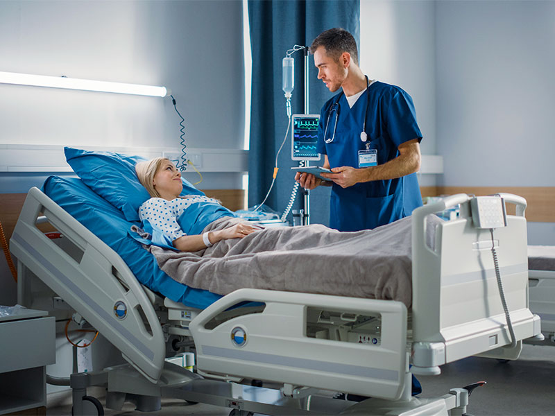 Como funciona a cirurgia para diminuir os seios? Mulher deitada na maca, conversando com o médico sobre a cirurgia para diminuir os seios
