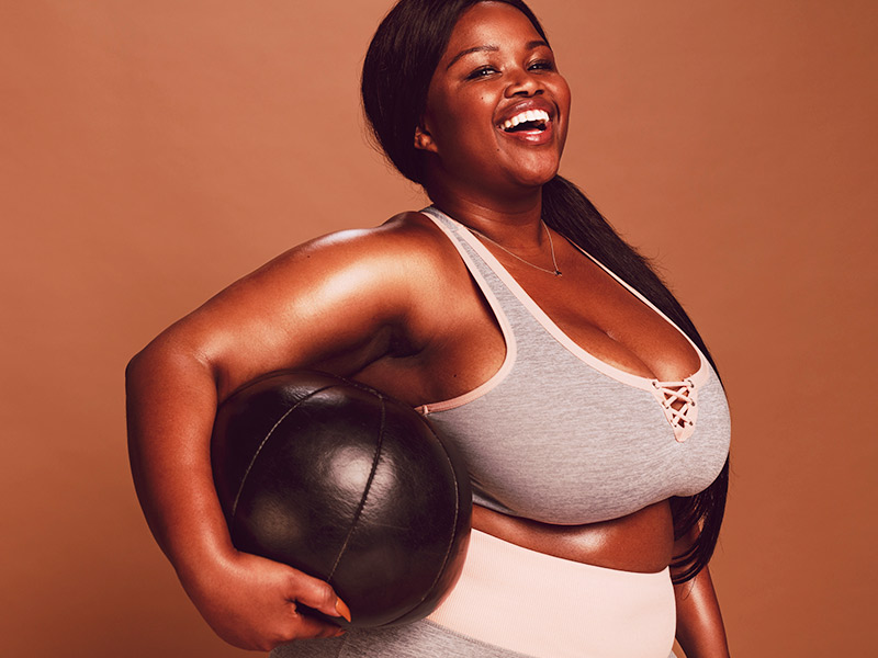 Mulher fazendo exercício para diminuir peito, com uma bola embaixo do braço