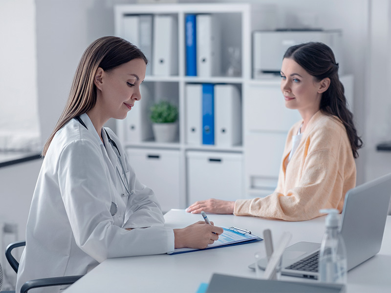 Paciente passando em consulta do pré-operatório da mastopexia com a médica, que está escrevendo em uma prancheta