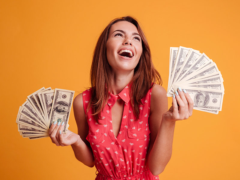 Imagem com fundo laranja e uma mulher segurando cédulas de dinheiro, expressando felicidade devido ao preço acessível da lipoescultura