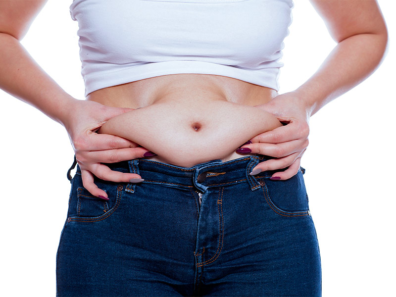 Após abdominoplastia quanto tempo para desinchar? mulher com mão na barriga inchaço pós cirurgia abdominoplastia