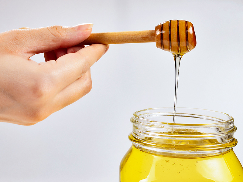 Mão pegando mel com colher de madeira, um dos remédios caseiros para tirar cicatriz