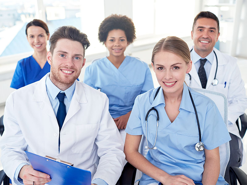 Imagem de uma equipe multidisciplinar, com profissionais da área de saúde, sendo três mulheres e dois homens. 