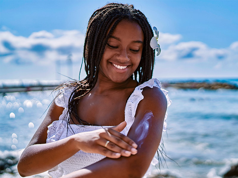 Mulher passando protetor solar na praia, depois de ter feito a redução de mama