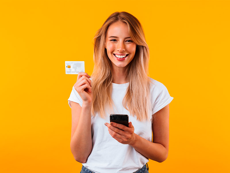 Mulher segurando um cartão de crédito e celular, feliz com o valor do lifting de mama