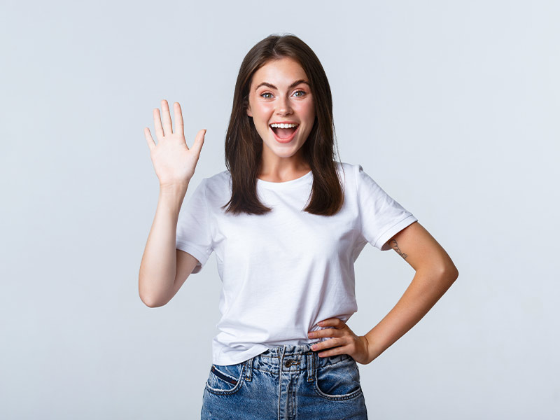 Mulher de camiseta branca e calça jeans dando tchau sorrindo