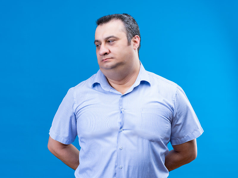 Homem de camisa azul de manga curta, olhando para a esquerda e com as mãos para trás