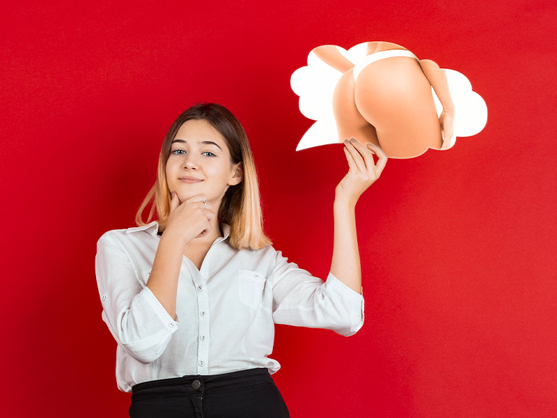 Imagem de uma mulher segurando um balão de pensamentos com a imagem de um bumbum com silicone nos glúteos