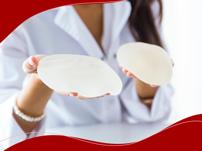 Como escolher uma clínica de silicone? Mulher de camisa branca segurando duas próteses, escolhendo qual a melhor clínica de silicone