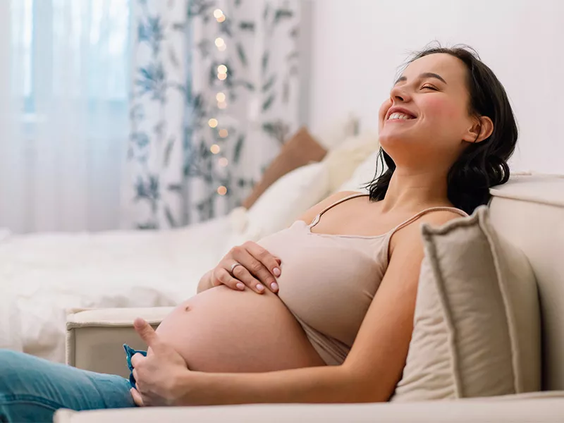 Grávidas podem usar produtos com esse ativo? Imagem de uma mulher grávida, sentada no sofá, com dúvida se pode usar ácido hialurônico