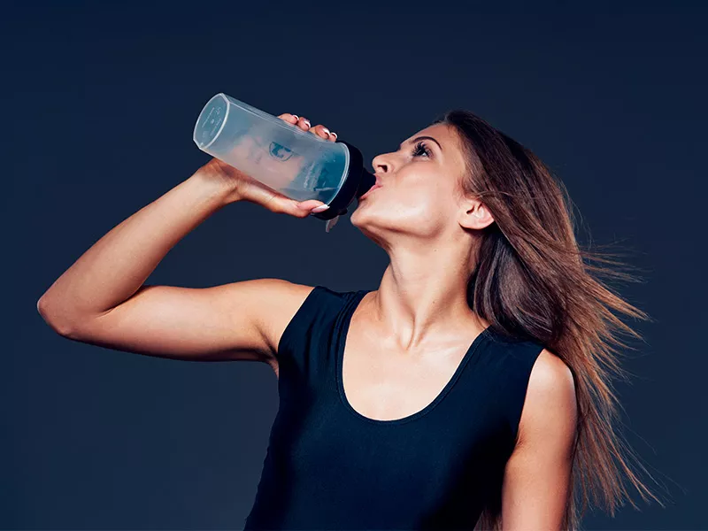 Os suplementos realmente funcionam? Imagem de uma mulher tomando ácido hialurônico em uma garrafa plástica