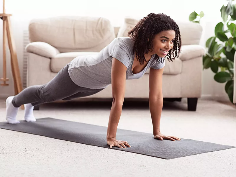 Exercícios para enrijecer os seios Mulher fazendo exercícios para firmar os seios em tapete de yoga na sala de casa