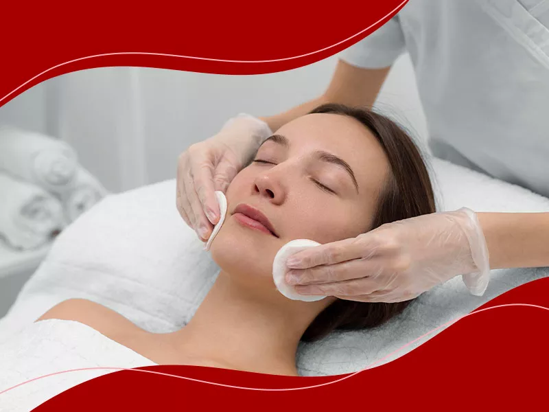 Mãos com luva segurando dois algodões redondos fazendo limpeza de pele no rosto de paciente para mostrar o que é limpeza de pele